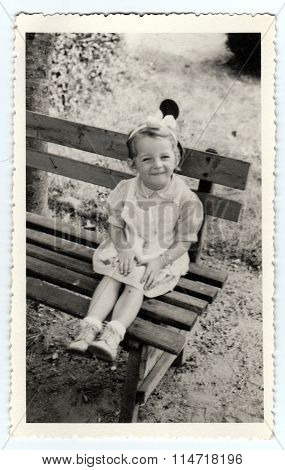 Vintage photo shows a small girl sits on a bench