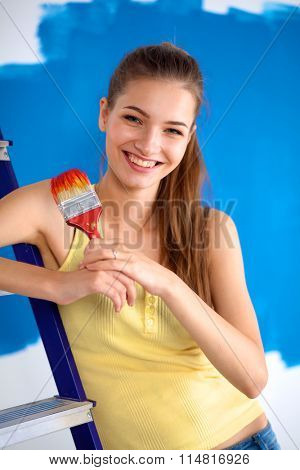 Beautiful young woman doing wall painting, standing near ladder