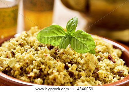 closeup of an earthenware bowl with couscous with vegetables, some ornamented glasses with tea and a golden teapot on a rustic wooden table