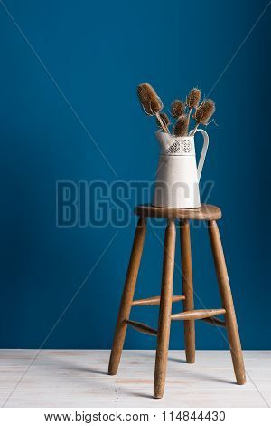 Old Pitcher Vase On A Stool Over Blue Backdrop