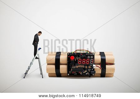 small businessman standing on the stepladder and looking at big bomb over light grey background