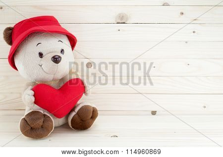 Bear In Love Wear Red Hat Hold Red Heart On Wooden Background.