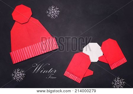 Origami red mitters and winter cap of paper on black board background