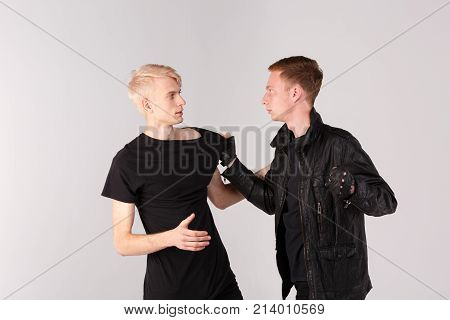 Two young guys fight. The brunette guy is holding the blonde guy by the T-shirt and swinging his fist at him. Isolation.