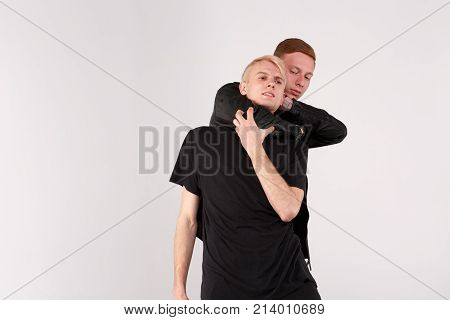 Two young guys are brunette and blond are fighting. A guy with dark hair dominates and does strangulation with the help of hand. Isolation.