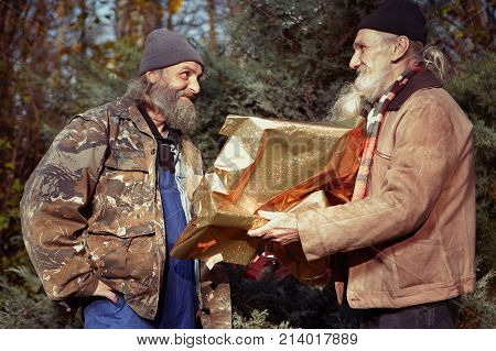 Two homeless older men celebrating christmas in park with gifts