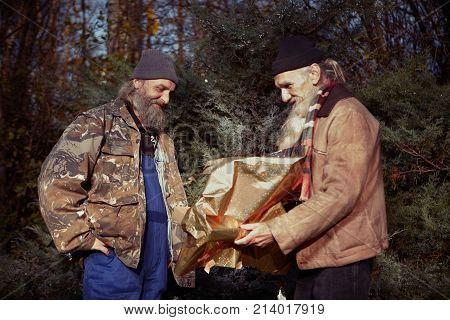 Two homeless older men celebrating christmas in park with gifts