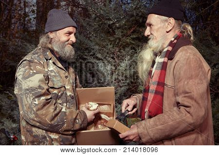 Two homeless older men celebrating christmas in park with gifts of food