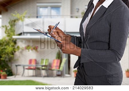 Close-up Of A Person's Hand Filling Document In Front Of House