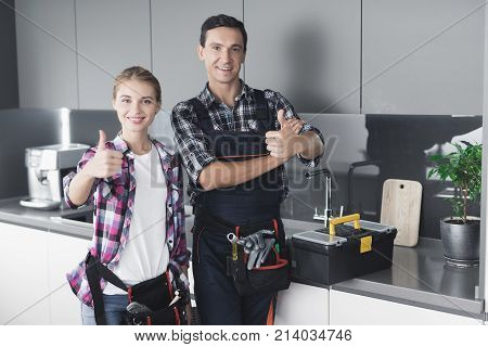 A man and a woman plumber will be cheated in the kitchen. They have just successfully repaired the sink for the customer. Next to them is a black box with a tool.