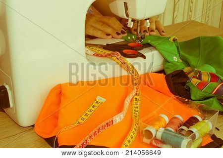 woman's hands using sewing machine with reels of colour threads. Workplace of tailor. people needlework and tailoring concept - tailor woman threading needle of sewing machine
