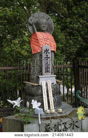 Nara, Japan -  May 31, 2017: Peaceful stone relegious Jizo statue with red skirt and a purificaton basin with ladles