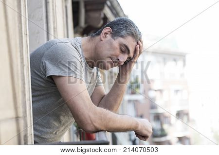 close up portrait of sad and depressed 40s man looking through outdoors at home balcony lonesome and thoughtful suffering depression thinking and feeling low in city buildings urban background