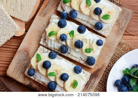Cottage cheese, bananas and berries sandwiches with crisp bread on wooden board. Great cottage cheese sandwiches recipe. Closeup