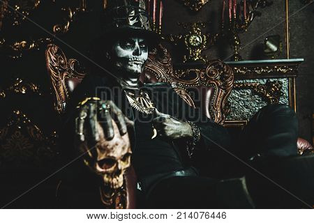 Halloween. A man with a skull makeup dressed in a tail-coat and a top-hat is in the old castle. Baron Saturday. Baron Samedi. Dia de los muertos. Day of The Dead. Old vintage interior.