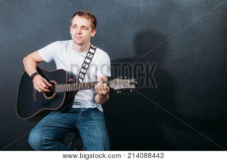 Cheerful young guitarist. Cheerful handsome young man playing guitar and smiling while sitting at chair