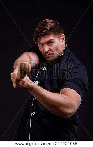 A man pumped up, confident in a black tunic holds the bats directed forward on a black background