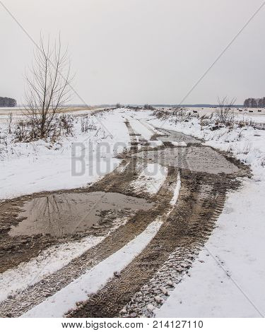 Traces of the tread of the car's wheels on the countryside snow-covered road in the field in the late autumn