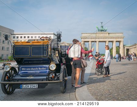 BERLIN GERMANY - AUGUST 25 2017; Neo-classical architectureof Barndenburg Gate in background selfie taking tourist by replica carriage on street with sign 