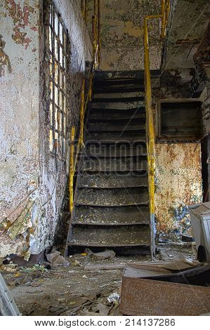 Stairs with yellow railing in a ruined industrial interior. Abandoned old factory.