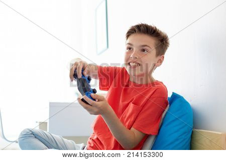 gaming, technology and people concept - smiling boy with gamepad playing video game at home
