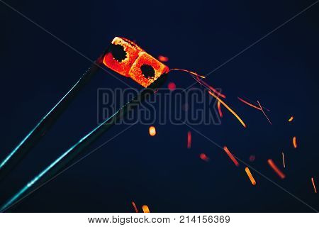 hookah coals with sparks in the glowing red hot tweezers close-up