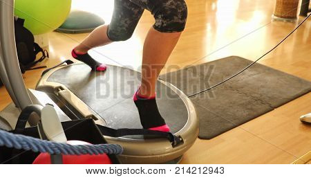 Slow motion half body of fit woman warming up in short leggings, training legs with thigh toner on the step. Modern gym defocused background. Female athlete warming up legs for cardio workout.