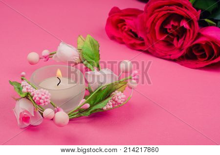 Burning candle and pink and red roses on a bright pink background (selective focus on the candle) copy space on the right