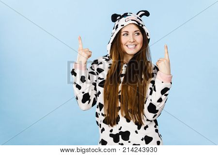 Happy teenage girl in funny nightclothes pajamas cartoon style pointing up with positive smiling face expression studio shot on blue. Advertisement concept
