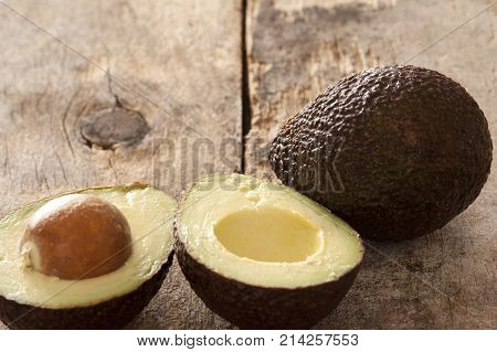 Tasty whole and halved ripe avocado pears with the pip still in forming a border with copy space on rustic wood