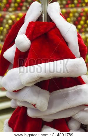 Santa Claus hat many in supermarket shop for sale hanging on the rack close-up