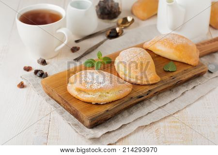 Pasties with cottage cheese and powdered sugar on a light wooden background. Traditional Russian pastry Sochnik. Selective focus. .