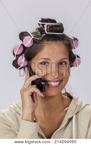 Portrait of a smiling young woman with hair curlers using a mobile phone.