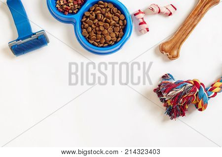 Dog care items, isolated on white background. Dry pet food in bowl, toy and bones. Top view. Copy space. Still life. Flat lay.