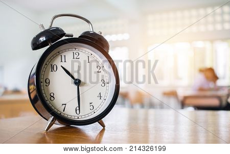 Closeup of Retro alarm clock with ten o'clock on table teacher in blur students exams classroom. Time is indefinite continued progress of existence. Education concept selective focus.
