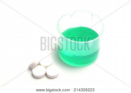 green medical liquid in a plastic cup with pills isolate on white