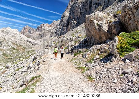 FUENTE DESPAIN - JULY 10 2016: Two tourists the man and the woman on a track in southeast a chachta of Picos de Europa the vicinity of Fuente De. Sunny day stone taluses traces from planes in the blue sky