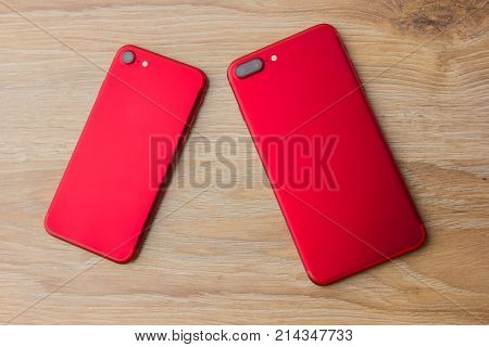 Two red phones on the desk. Smartphones of red color lie on a wooden table.