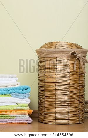 Basket for laundry in the bathroom. Wicker basket next to a stack of colored towels. Capacity for dirty laundry.