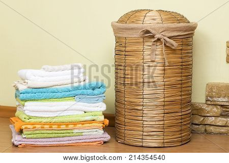 Basket for laundry in the bathroom. Wicker basket next to a stack of colored towels. Capacity for dirty laundry.