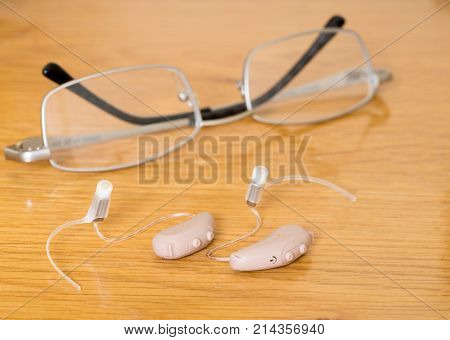 Macro close up of a matched pair of tiny modern hearing aid on wooden bedside dressing table