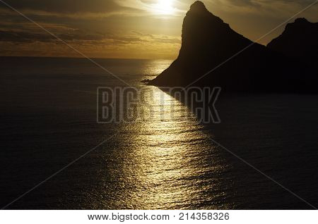 Eerie sunset showing streak of light over ocean with black mountain silhouette