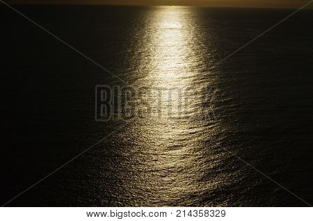 Eerie sunset showing streak of light over ocean with black mountain silhouette