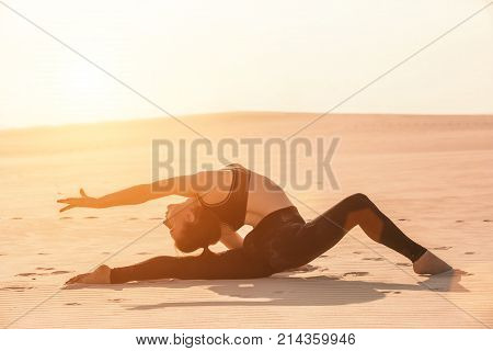 Fitness yoga woman stretching on sand. Fit female athlete doing yoga pose before running training outside in amazing landscape.
