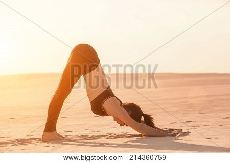 Fitness yoga woman stretching on sand. Fit female athlete doing yoga pose before running training outside in amazing landscape.