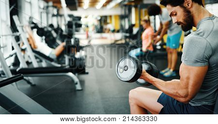 Muscular bodybuilder guy doing exercises with dumbbells in gym