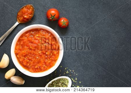 Homemade traditional Italian marinara or pomodoro tomato sauce made of fresh tomato garlic dried oregano and salt served in bowl with ingredients on the side photographed overhead on slate with natural light (Selective Focus Focus on the top of the sauce)