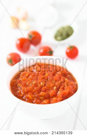 Homemade traditional Italian marinara or pomodoro tomato sauce made of fresh tomato garlic dried oregano and salt served in bowl with ingredients in the back photographed on white wood with natural light (Selective Focus Focus in the middle of the sauce)