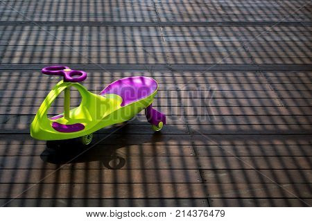 The children's car/scooter in striped shadows on wooden floor outdoor