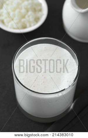 Fresh homemade kefir drink in glass kefir grains and milk in the back photographed with natural light (Selective Focus Focus one third into the kefir drink) (Digitally Altered: Desaturated Image)